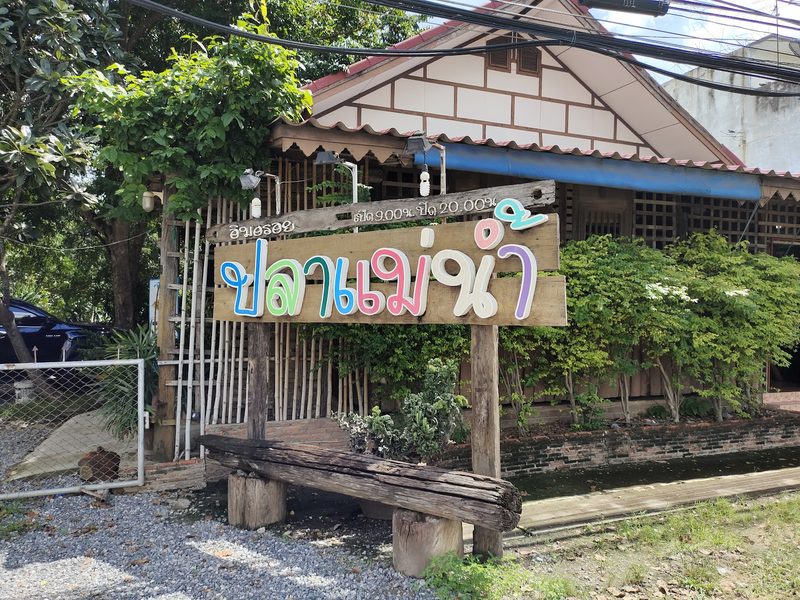 ป้ายไม้ริมถนนตัวอักษรหลากสี ปลาแม่น้ำ หน้าสวนของร้าน