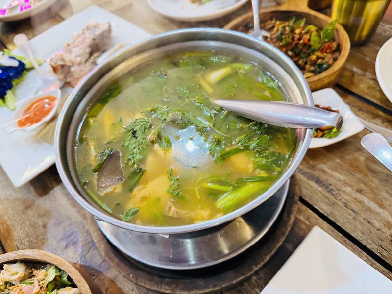 หม้อต้มปลาน้ำใสบนโต๊ะไม้ มีกับข้าวอื่นรอบ ๆ